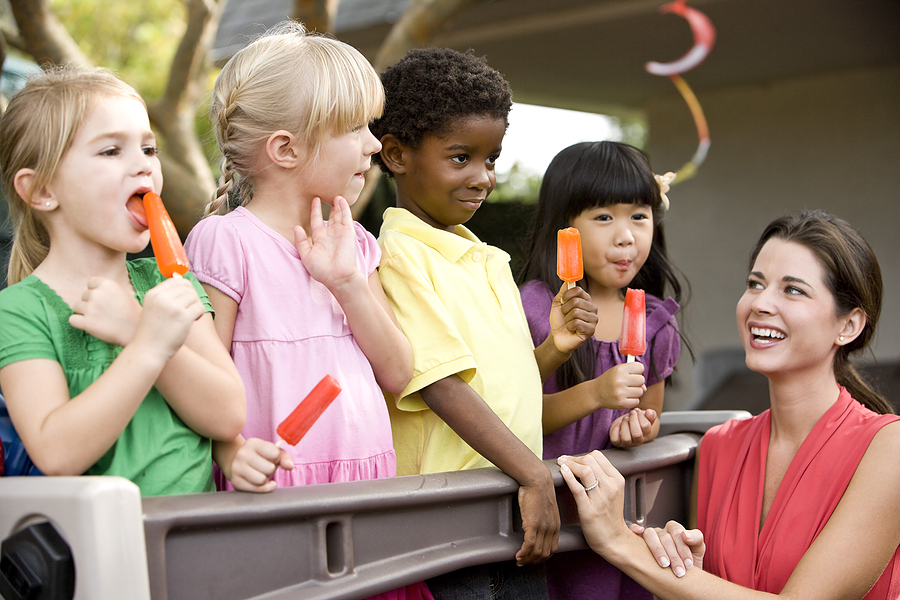 Children at the playground enjoy popsicles with their teacher